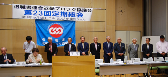 近畿ブロック協議会役員の紹介（各府県会長ほか）。 「演壇」後方から有元・大阪退職者連合会長、右隣　同　林・事務局長、増田・滋賀退職者連合会長、高原・兵庫退職者連合会長・中村・和歌山退職者連合会長、奥田・京都退職者連合会長、奈良退職者連合会長、松尾退職者連合会長、他（両サイドは幹事）